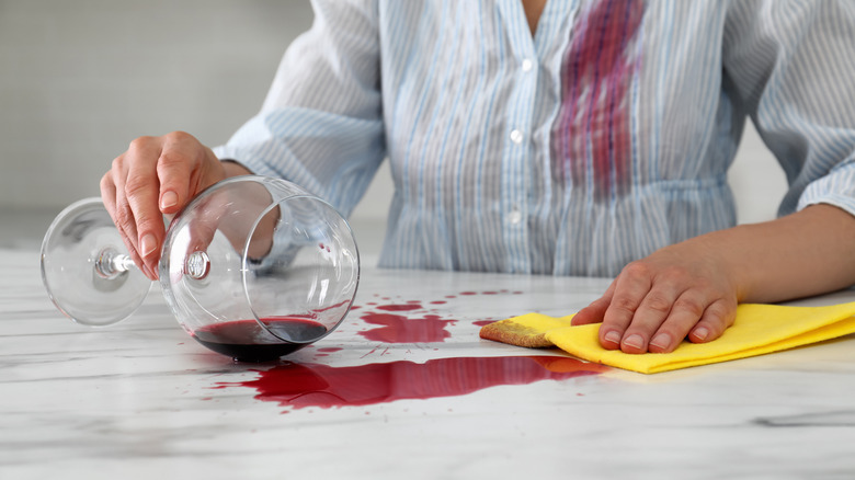 A person cleaning up red wine spilled on a white marble countertop