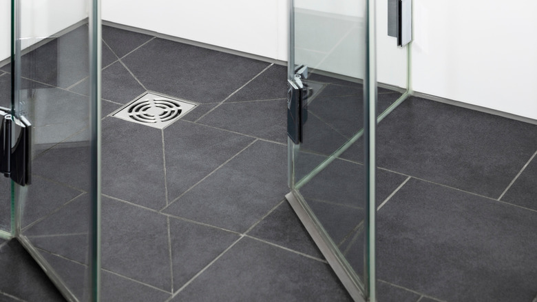 A black tiled shower floor with a chrome drain and glass doors opening out