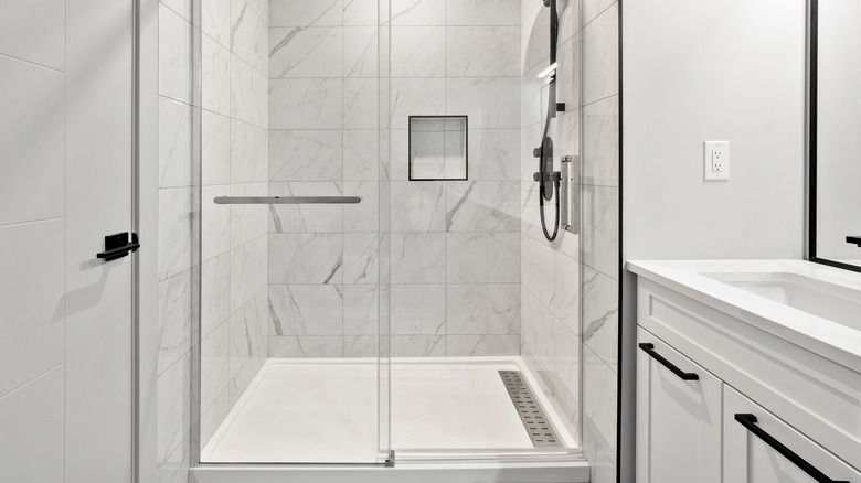 An all-white bathroom with black accents and marbled tiles inside the shower