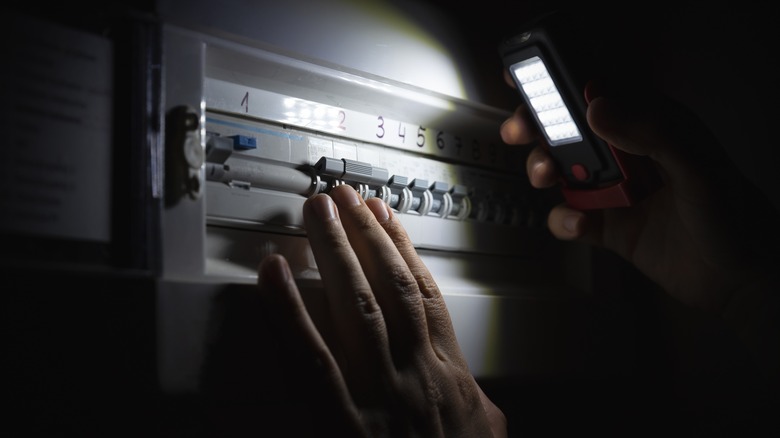 A person shininig a flashlight over a breaker box