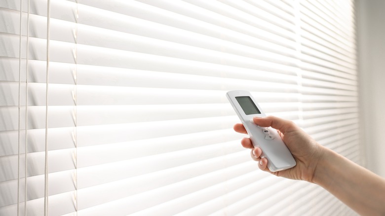 A person pointing a remote at white blinds