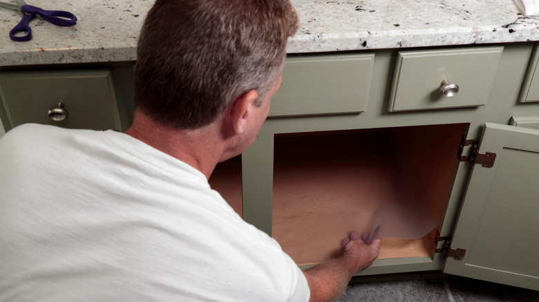 A man placing clear shelf liner under bathroom cabinet.