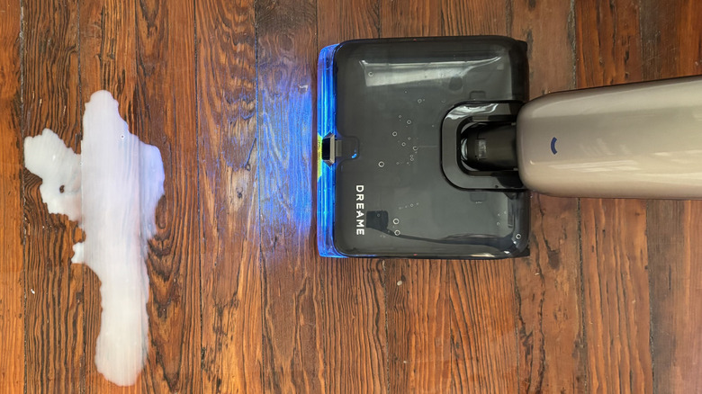 A Dreame Aero Ultra Steam Vacuum Mop in use angled towards a puddle of milk on the floor