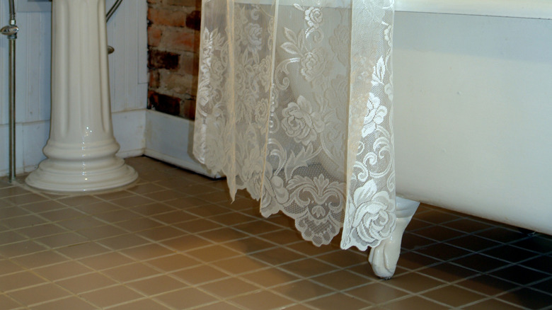 A lace privacy curtain used as a shower curtain around a vintage claw foot bathtub.