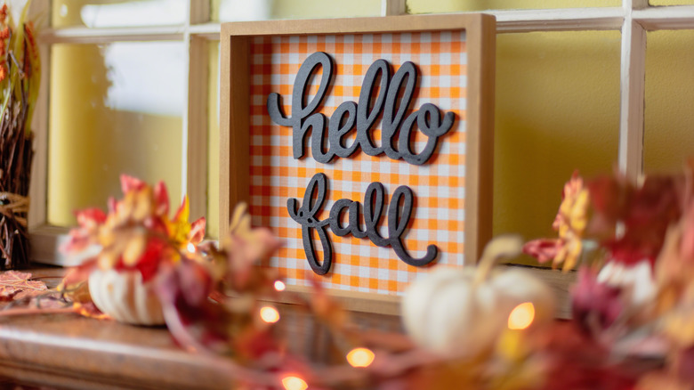 A shelf decorated with fall decor and a "hello fall" sign.