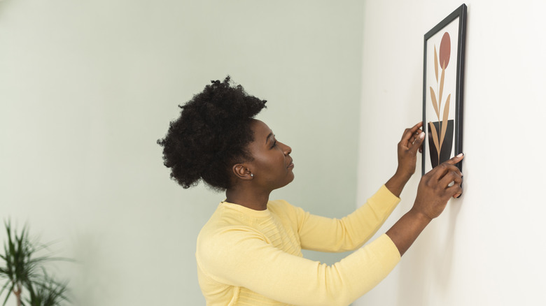 A woman hangs artwork in her bathroom