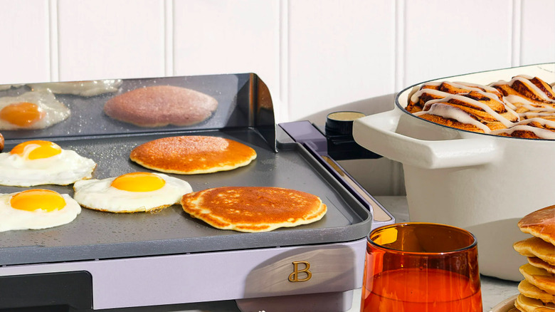 Electric griddle with pancakes and eggs on it.