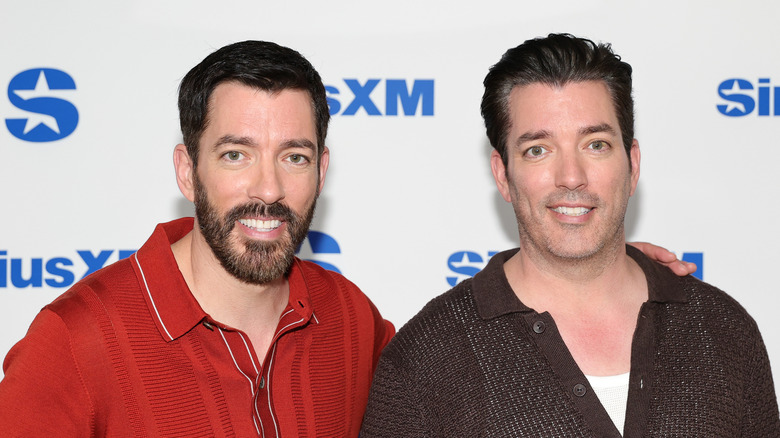 Drew Scott and Jonathan Scott pose together in front of a media wall