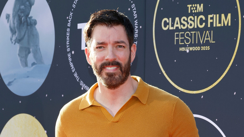 Drew Scott in a yellow shirt standing in from of a Classic Film Festival board squinting at the camera