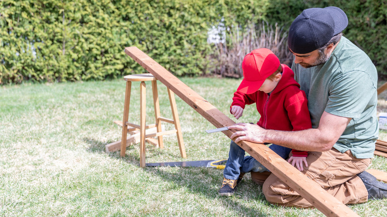 A father and small son measuring a piece of wood in backyard