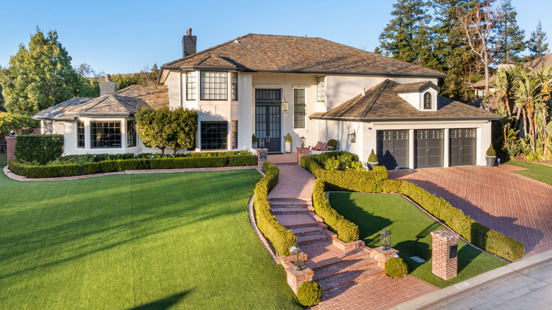 Large traditional home with brick driveway and manicured lawn with hedges