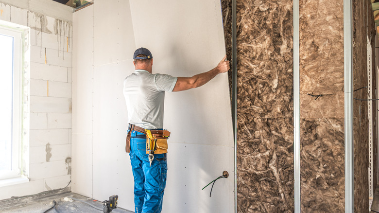 A worker is laying drywall board on a metal support structure of partition.
