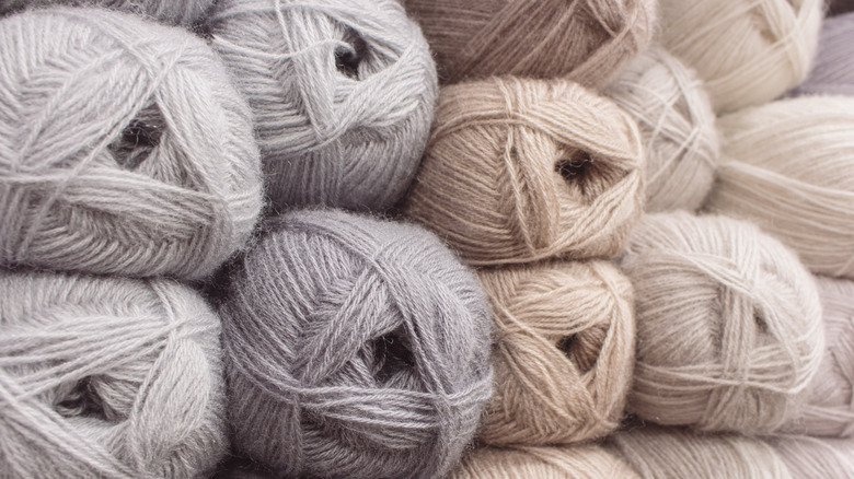 Gray, beige, and cream colored skeins of yarn are stacked together.