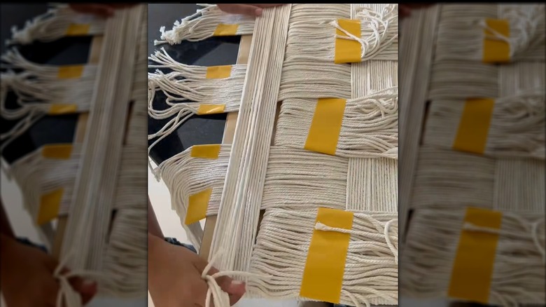 A pair of hands weaves and attaches sections of yarn on a piece of cardboard.