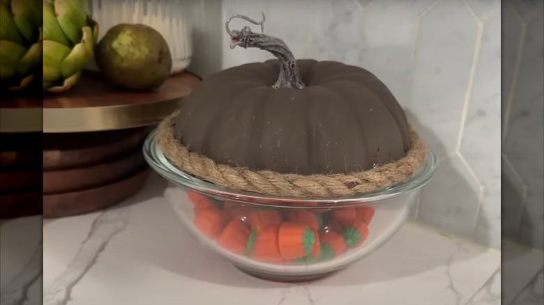 A Dollar Tree DIY faux pumpkin lid on top of a glass bowl filled with candy