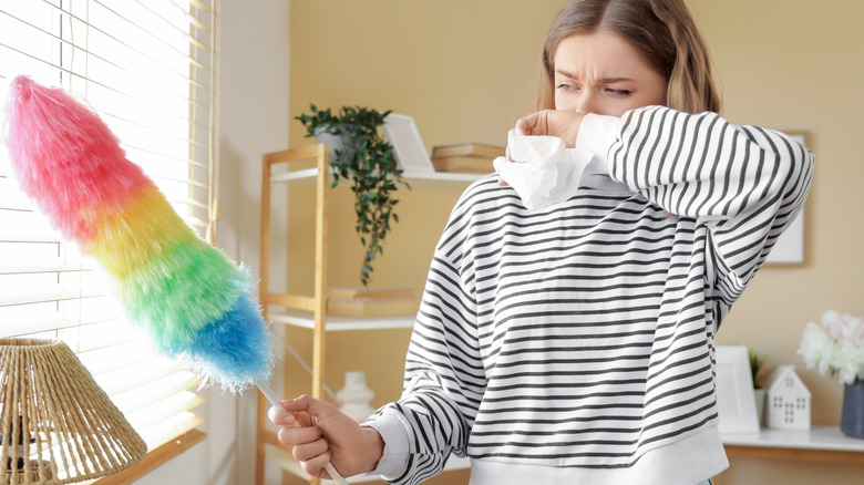 woman sneezing while dusting