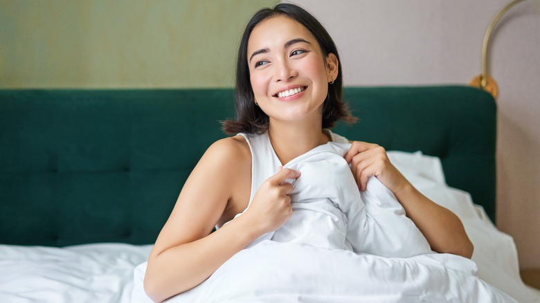 Woman in bed smiling and holding duvet