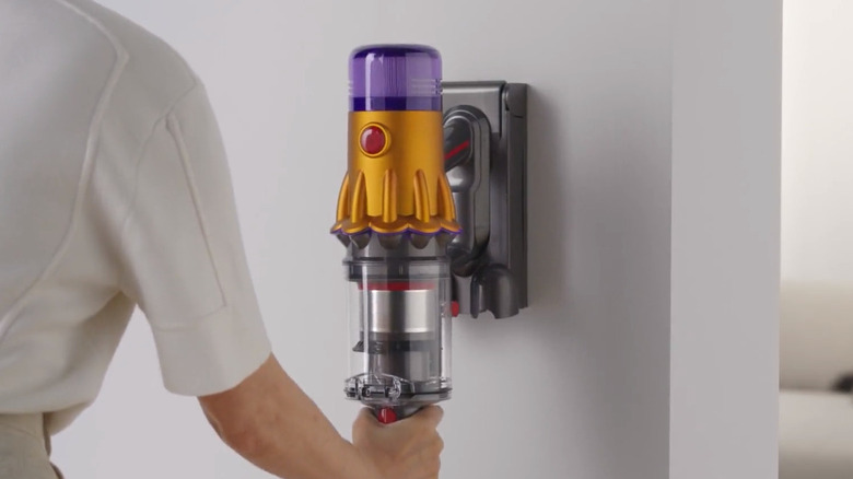 A person hanging up the Dyson V12 Detect Slim on a wall