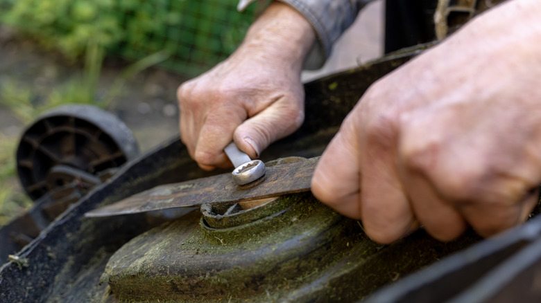 A pair of hands removing the bolt on a mower blade