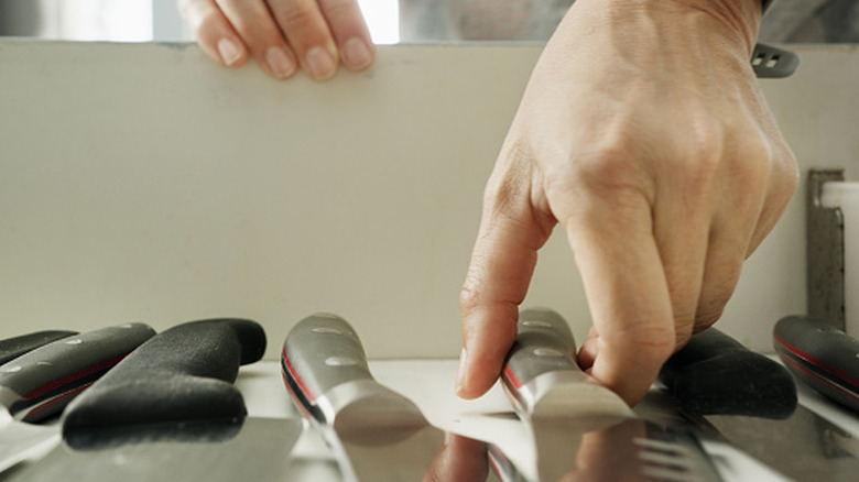 Close-up of a woman's hands picking up a knife from kitchen drawer