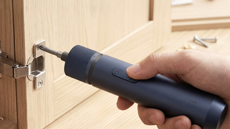 Cordless electric screwdriver tightening a screw on a cabinet hinge
