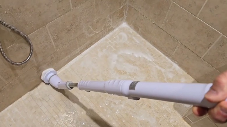 A person using the Tuyu Electric Spin Scrubber to clean a shower wall