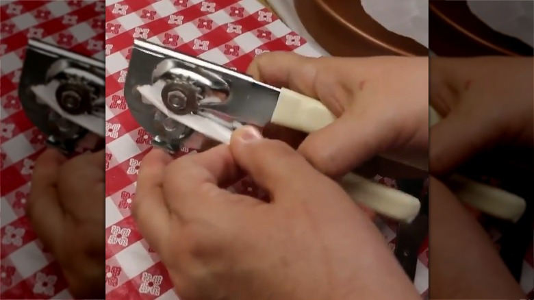 Hand inserting a strip of wax paper into a can opener's blade