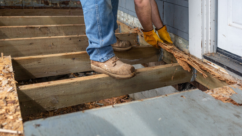 A person standing on the joists of a deck while pulling off old wood