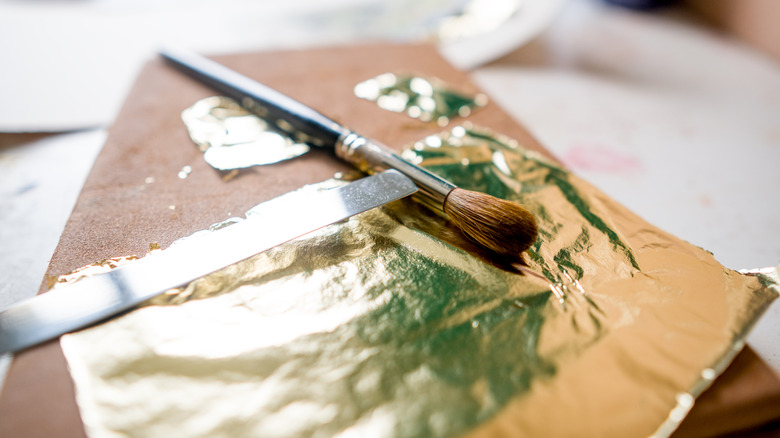 close up of gold leaf sheets next to a paintbrush