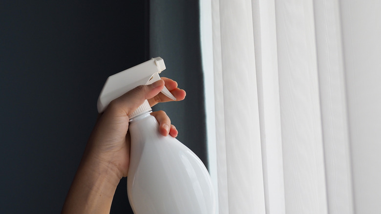 Hand holding a white spray to mist white linen curtains against a dark-colored background