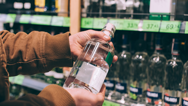 Man in brown sweatshirt holds a bottle of vodka to look at the label in a grocery store
