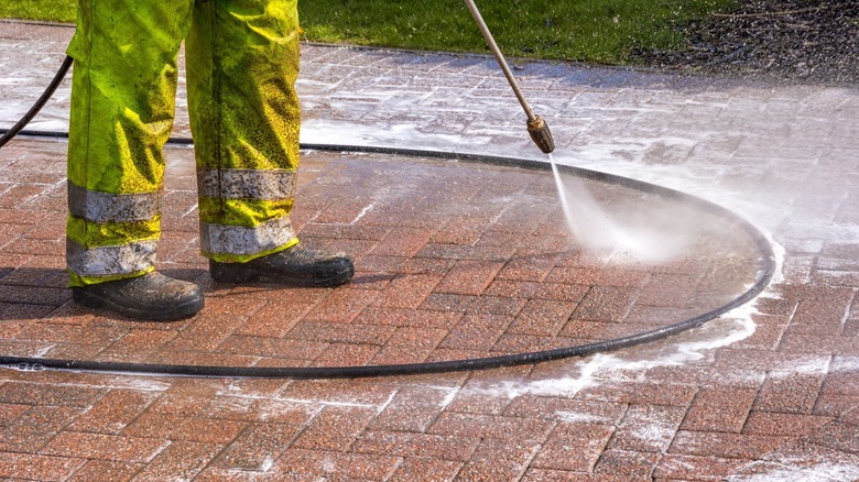 Man pressure washing brick paver patio