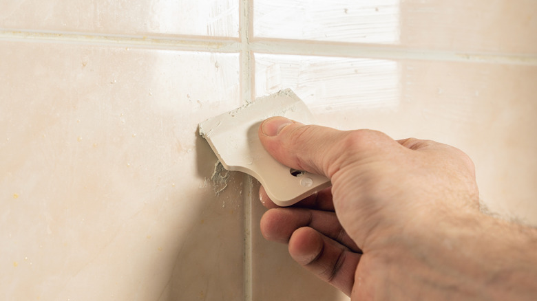 Hand applying grout between shower wall tiles to repair crack