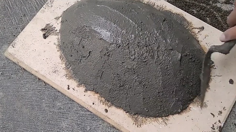 A person smoothing the cement on a concrete planter using a flat trowel.