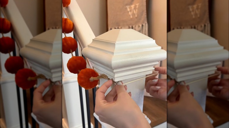 A pumpkin garland being hung on a banister with a rubber band.