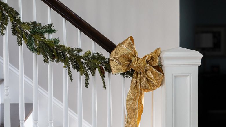 A green garland hanging from a banister with a gold bow.