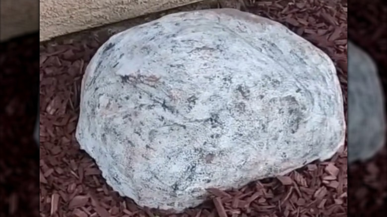 A plastic bowl covered in a faux stone surface hides a pipe outlet in a yard.