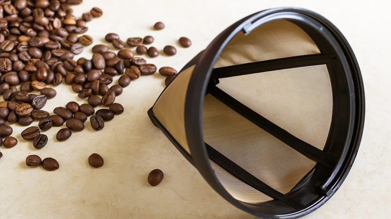 Reusable coffee filter and coffee beans spread on an off-white surface