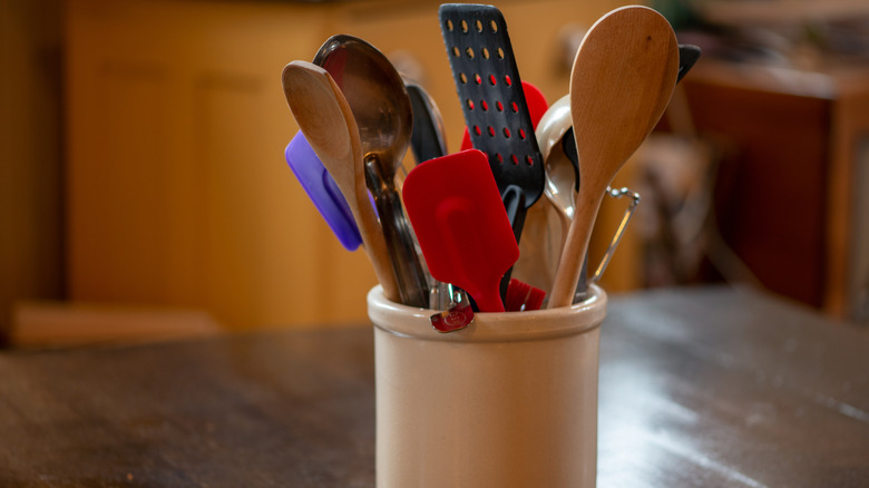 A kitchen utensils caddy sits on a dark wooden table.