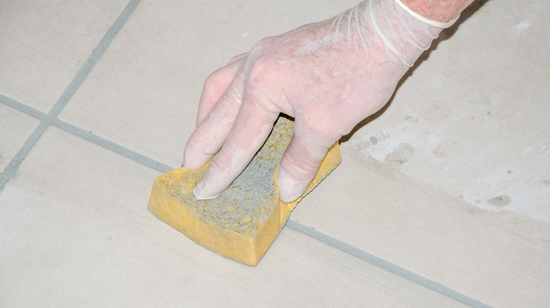 A person's hand wiping grout with a sponge