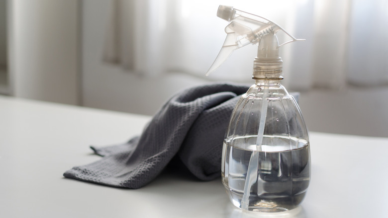 A spray bottle filled with distilled white vinegar and water with a gray cloth placed in the background