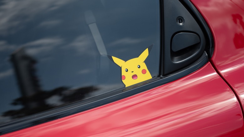 A cartoon decal on a window of a red car.