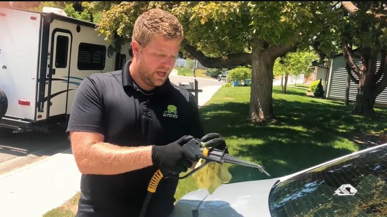 Man holding a steam cleaner in front of a car with a sticker on the rear windshield