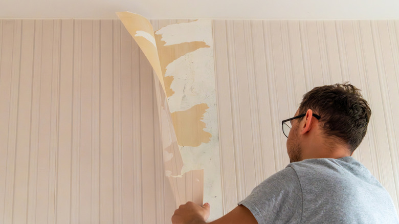 man peeling wallpaper off wall