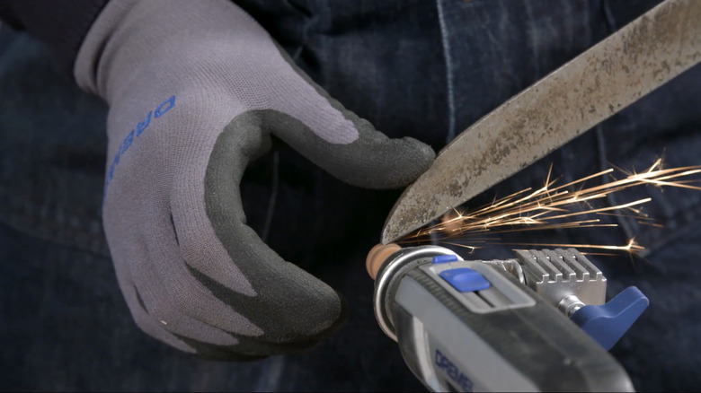 A person wearing gloves sharpening shears with a Dremel.