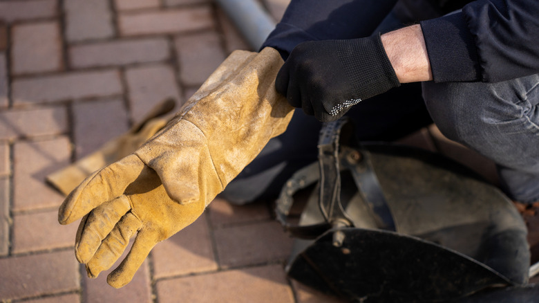 A man putting on protective leather gloves.