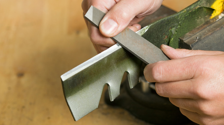 Person using a file to sharpen the edge of a mower blade