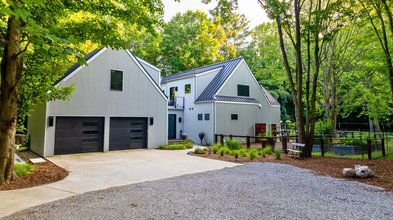 Modern house surrounded by trees with a concrete and gravel driveway