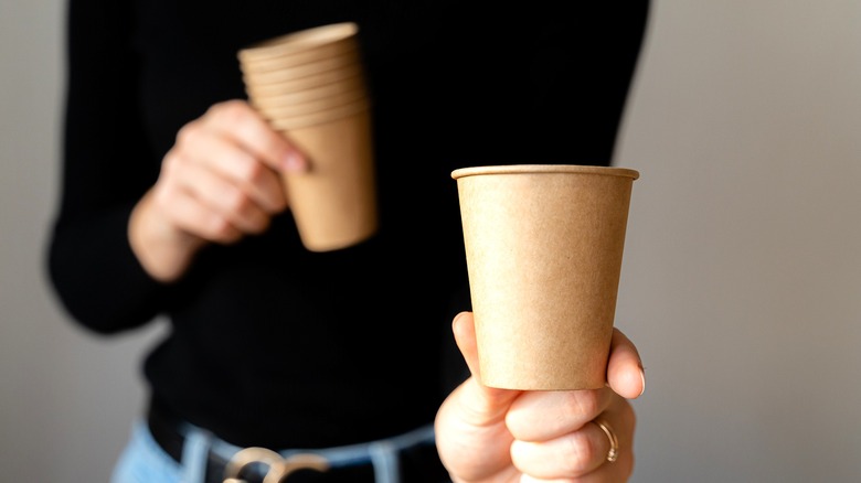 A person holding a few brown paper cups
