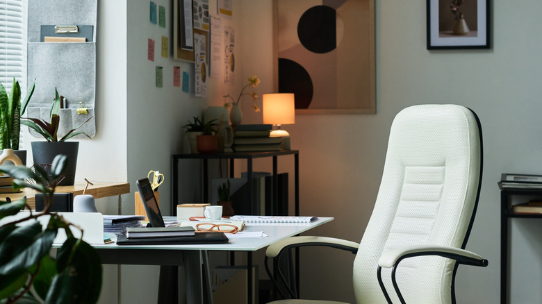 Home office with a cosy lamp warming up a dark corner next to the desk, with a white leather office chair in the foreground